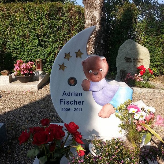 Kindergrabmal in Mondform mit Sternen und einer Bärenfigur, davor rote Rosen und Blumen.