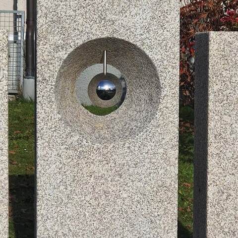 Heller Granitpfeiler mit einem gebohrten Trichter, darin eine spiegelnde Kugel.