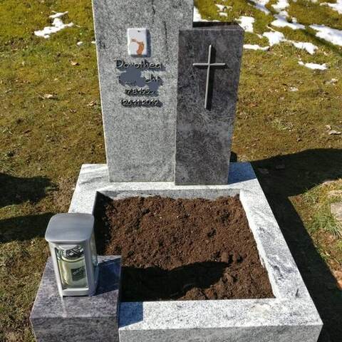 Zweiteiliges Grabmal aus hellem und dunklem Granit mit eingelassenem Bildfeld, aufgenommen im Winter.