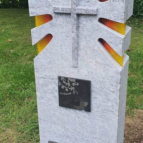 Helle Stele mit eingearbeitetem Kreuz und gelb-roten Glasstrahlen.