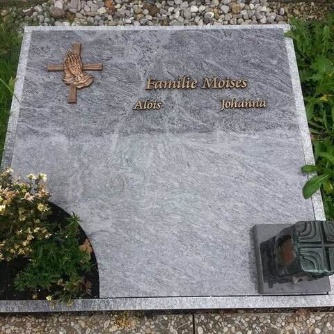 Große helle Liegeplatte mit aufgesetztem Bronzekreuz und ausgespartem Pflanzfeld.