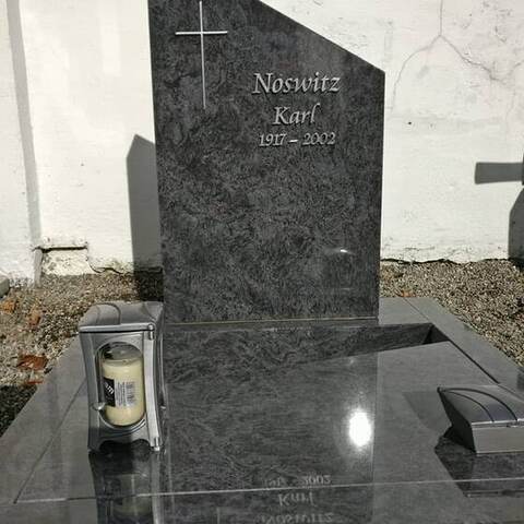 Hoch poliertes dunkles Grabmal mit eingehauenem Kreuz und heller Schrift, davor eine Abdeckplatte.