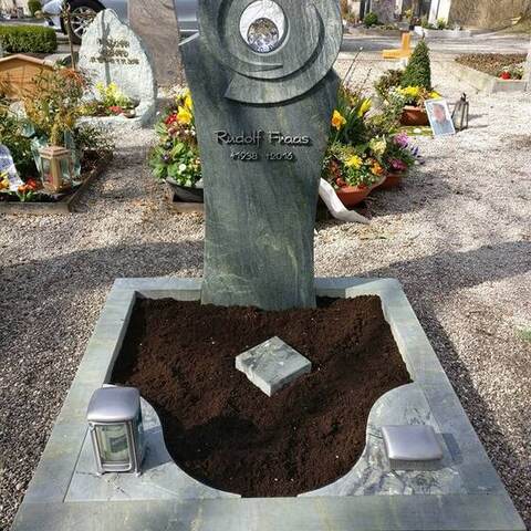 Bogenförmige Stele aus grünlichem Stein mit einem eingelassenen Metallring und einer Kugel.