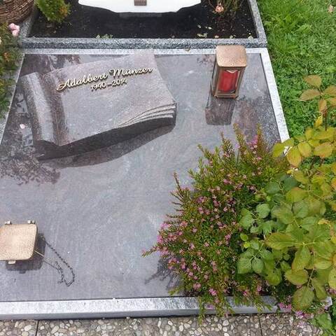 Liegeplatte aus hellem Granit mit einem plastisch herausgearbeiteten, aufgeschlagenen Buch.