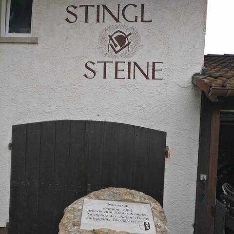 Hauswand der Werkstatt mit dem gemalten Schriftzug Stingl Steine und dem Steinmetz-Zunftzeichen, darunter ein Holztor.
