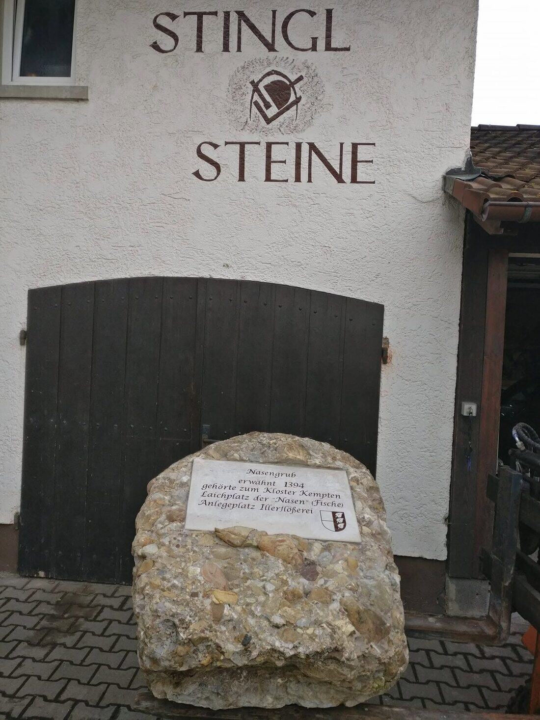 Hauswand der Werkstatt mit dem gemalten Schriftzug Stingl Steine und dem Steinmetz-Zunftzeichen, darunter ein dunkles Holztor und der Gedenkstein zur Nasengrub.